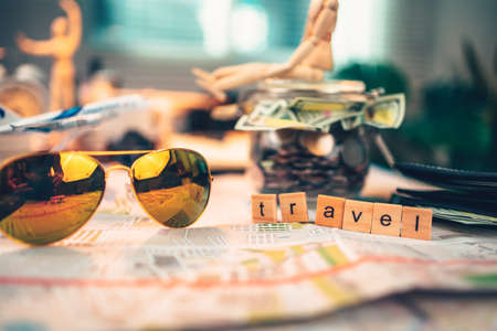 Wood square with word "travel", sun glasses and  money in jar on the map. travel plan concept.の写真素材