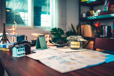 Saving money in glass jar for travel, holiday, vocation on dairy and map on the table. Travel budget concept.の写真素材