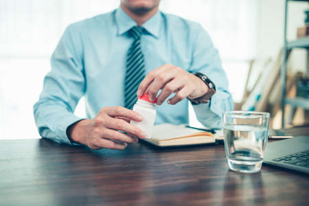 Business man open bottle pill and water glass on the table.の写真素材