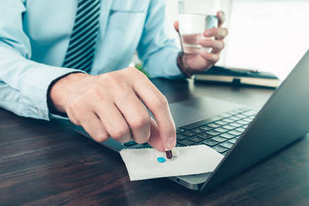 Businessman working with glass of water takes pill. Working and sick concept.の写真素材