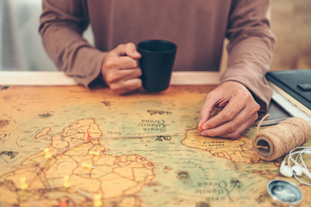 Tourist planning vacation, holiday with the help world map. Man's hand marks route on map and using...
