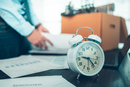 Alarm clock on the table and unemployed keep document and laptop into cardboard box.  Quiting a job, businessman fired or leave a job concpet.の写真素材