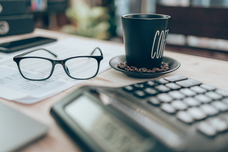 Cup of coffee and glasses on table and Accountant working on calculator to calculate company data,...