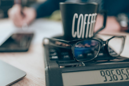 Cup of coffee and glasses on calculator and Accountant working on calculator to calculate company...