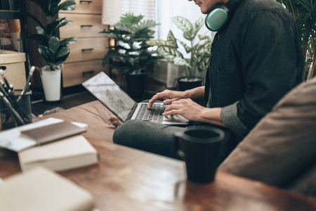 Travelers planning trips and use laptop to book hotels, buy plane tickets, search map, or find travel routes on sofa bed in living room at home. Travel concept.の写真素材