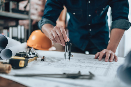 Engineering working with drawings inspection and writing on the office desk and Calculator, triangle ruler, safety glasses, compass, vernier caliper on Blueprint. Engineer, Architect, Industry and factory concept.の写真素材