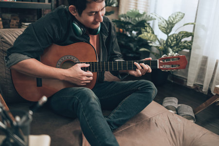 young man relax and playing guitar while sitting on sofa bed in living room at home.