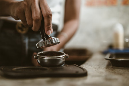 Barista using a tamper to press ground coffee into a portafilter. Coffee maker concept.の写真素材