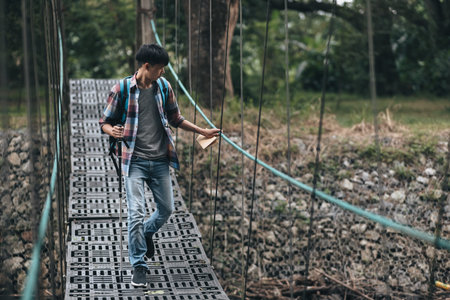 Hikers use trekking pole with backpacks and hold map walking through the bridge in the forest....