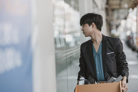 An employee fired or resigned from a company is holding a box reading a job posting in front of the company.
 Unemployed, hiring job, quitting job concept.の写真素材