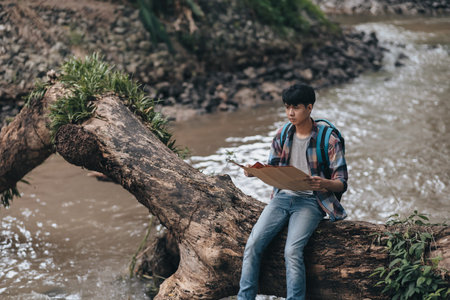 Lost hiker with backpack checks map to find directions near the river in the forest. hiking and...