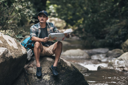 The trekker was looking at the map in his hand to find the hiking trails at the stream in the...