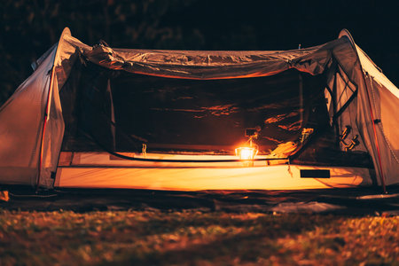 A gas lamp is on the tent floor at night and a bag with a ukulele and shoes next to it. Camping equipment, vocation and travel concept.の写真素材