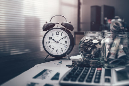 Alarm clock, Stack of money coin for saving money growing business, saving plan. Calculator, pen, business graph in workplace. Business and finance concept.の写真素材