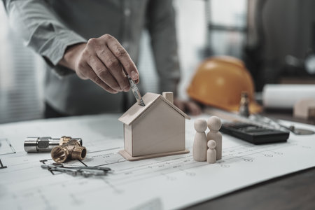 Architect hand putting money into house money box on blueprint house plan design represent family keep money to buy house. Cost Architect and engineer concept.の写真素材