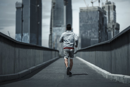 A man running up on footbridge in the city center park for cardio workout.  Health and Lifestyle in big city life concept.の写真素材