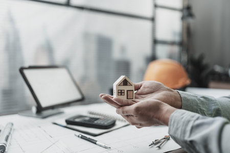 Architect engineer hands hold and protect mini house model on blueprint.  Sell, Protect House, cost planning design and construction concept.の写真素材