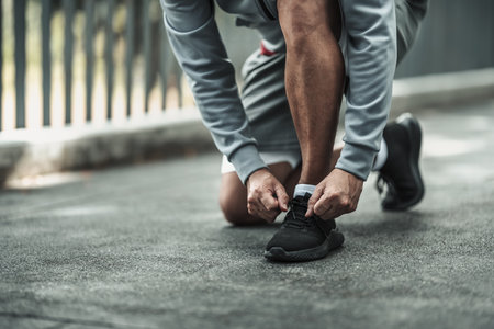A man tying shoelaces on sport shoes in the city center park before cardio workout, running.  Health and Lifestyle in big city life concept.の写真素材