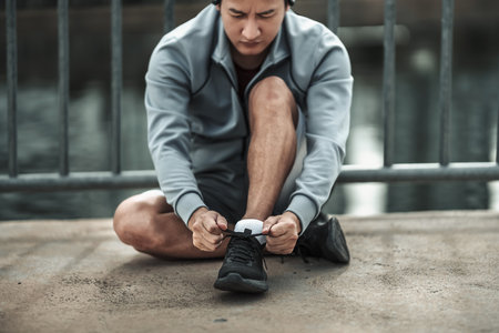 A man tying shoelaces on sport shoes in the city center park before cardio workout, running.  Health and Lifestyle in big city life concept.の写真素材