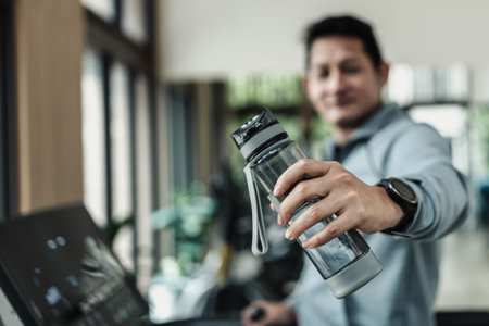 A man hold water bottle on treadmill in gym. Fitness, gym, workout and lifestyle concept.