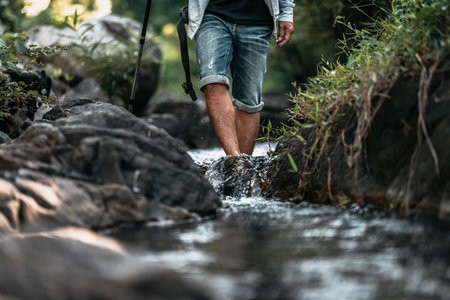 Hikers walk on rocks in the stream flowing from the waterfall in the forest.の写真素材