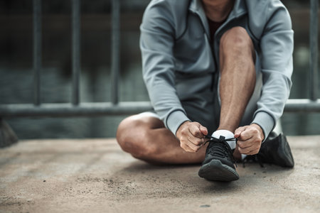 A man tying shoelaces on sport shoes in the city center park before cardio workout, running.  Health...