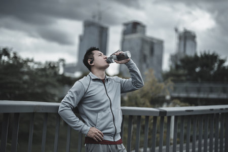 Young sport man drink water after jogging, running in the park. Sport thirsty and resting after exercise. Health and Lifestyle in big city life concept.の写真素材