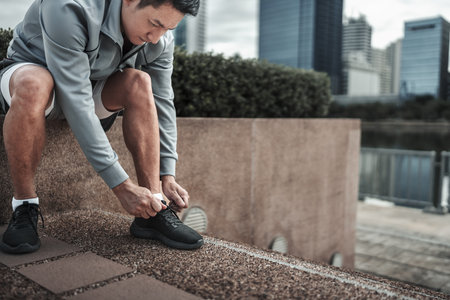 A man tying shoelaces on sport shoes in the city center park before cardio workout, running.  Health and Lifestyle in big city life concept.の写真素材