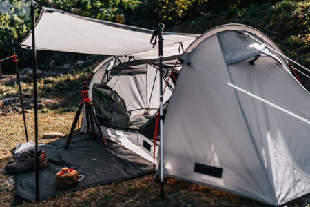 hiking bag in tent and gas with stove, hiking shoes, trekking pole and tripod on the ground. tents pitched on hillsides beside streams of water from waterfalls.の写真素材