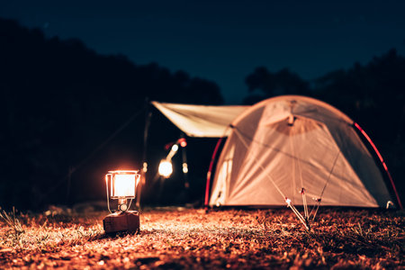 Gas lantern on the ground in front of tents pitched on hillsides beside streams of water from waterfalls at night under star in the sky.の写真素材