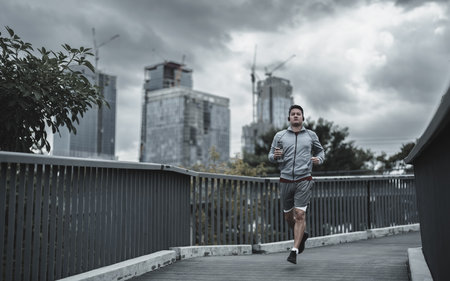 A man holding a water bottle and running up on footbridge in the city center park for cardio workout.  Health and Lifestyle in big city life concept.の写真素材