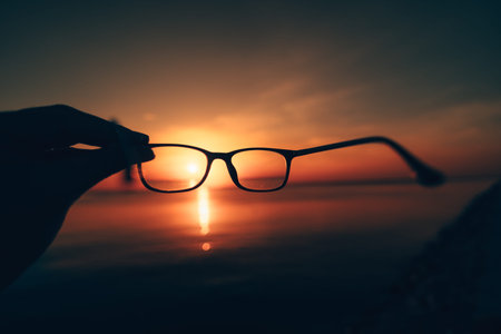 Hand Reaching Towards the Sunset Over a Calm Ocean Horizon