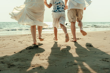 On vacation, travel, or a long weekend, spend time together with family and have fun and happiness by running hand in hand on a beautiful beach with sunset light.の写真素材