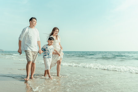 On vacation, travel, or a long weekend, spend time together with family and have fun and happiness by walking hand in hand on a beautiful beach with sunset light.の写真素材