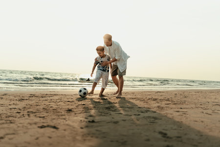 Father and son play football happiness on the beach during vacation, travel, long weekend, summer or any other holiday. They are happy to spend time together.の写真素材