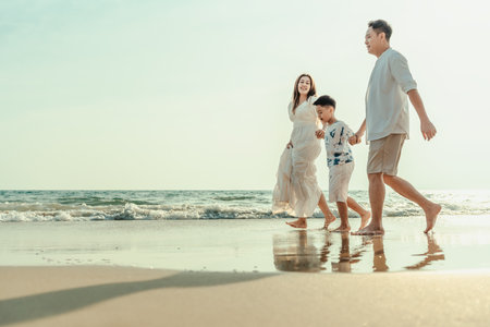 On vacation, travel, or a long weekend, spend time together with family and have fun and happiness by walking hand in hand on a beautiful beach with sunset light.の写真素材