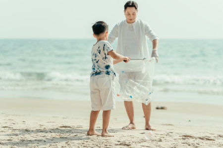 On the beach, a father and son carry bags to collect trash. Clean up the dirty sea or ocean and collect reusable plastic bottles. Garbage recycling.の写真素材