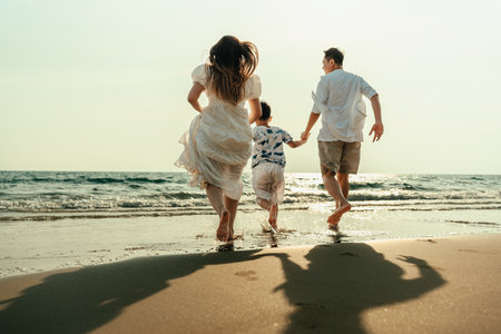 On vacation, travel, or a long weekend, spend time together with family and have fun and happiness by running hand in hand on a beautiful beach with sunset light.の写真素材