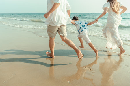 On vacation, travel, or a long weekend, spend time together with family and have fun and happiness by running hand in hand on a beautiful beach with sunset light.の写真素材