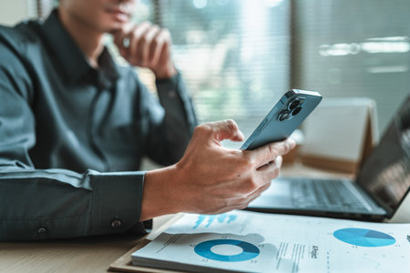 Businessman uses mobile phone to check news, email, market information, stocks while working with laptop in Office.の写真素材