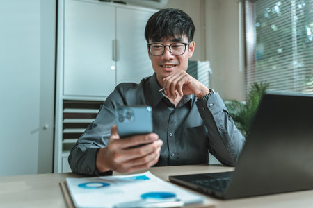 Businessman uses mobile phone to check news, email, market information, stocks while working with laptop in Office.の写真素材