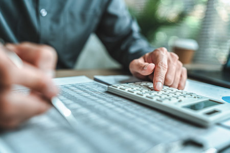 An accountant is seated at a desk in the office, utilizing a calculator to determine balances, profits, currency conversions, and costs. This involves various accounting and financial concepts.の写真素材