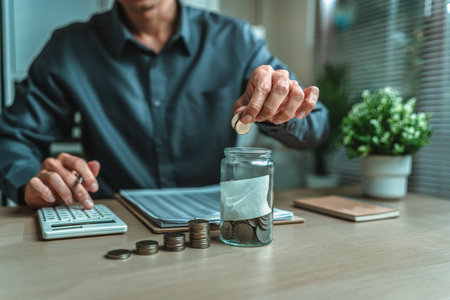 Businessman putting coins saving money with jar coin on desk. income, deposit, financial planning and investment concept.の写真素材