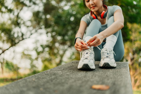 A woman dressed in workout clothes is tying her shoelaces, preparing to go for a run and exercise at the park.の写真素材