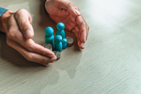 Businessman's hand gestures to protect money and wooden dolls represent family. Image represents the concept of asset protection, emphasizing safeguarding financial investments and propertyの写真素材