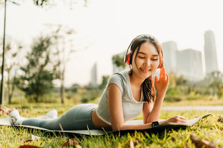 A woman dressed in workout clothes is wearing headphones and listening to music while resting between sets of abdominal exercisesの写真素材