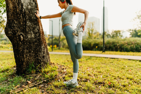 A woman dressed in workout clothes is wearing headphones and listening to music while stretching her muscles before exercising, before running, or after exercising.の写真素材