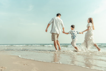 On vacation, travel, or a long weekend, spend time together with family and have fun and happiness by running hand in hand on a beautiful beach with sunset light.の写真素材