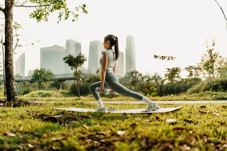 A woman dressed in workout clothes is wearing headphones, listening to music, and performing squats with dumbbells to exercise her legs and glutesの写真素材