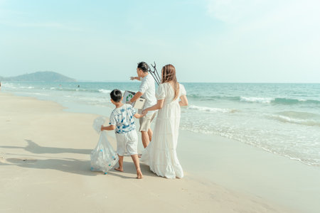 Happy Asian family collecting trash on the beach. Father holding a recyclable trash box, child holding a garbage bag with plastic bottles.の写真素材